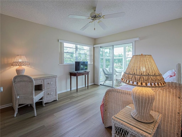 living area featuring healthy amount of natural light, wood finished floors, a textured ceiling, ceiling fan, and baseboards