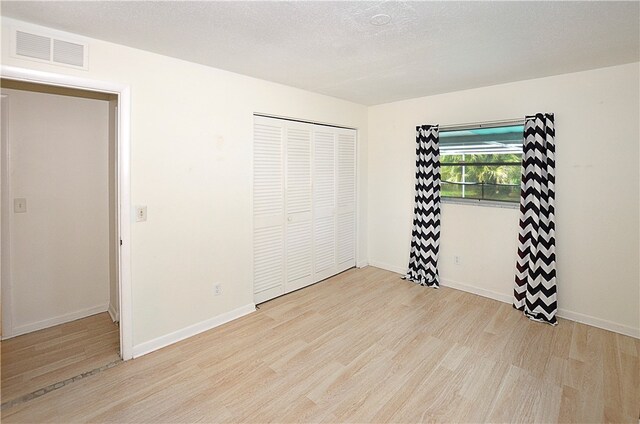 unfurnished bedroom featuring a textured ceiling, a closet, and light hardwood / wood-style flooring