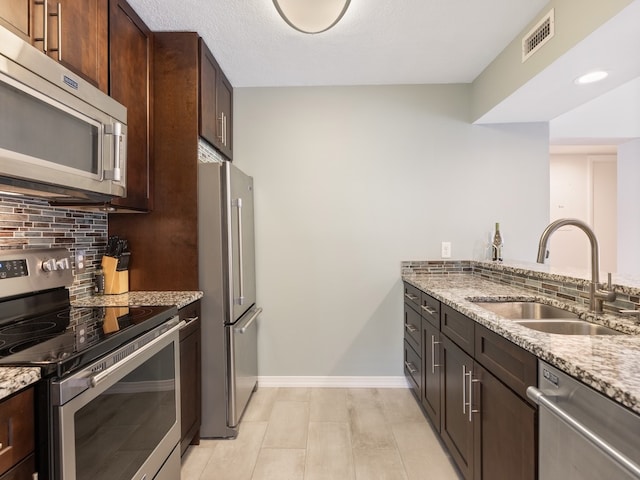 kitchen featuring stainless steel appliances, sink, backsplash, and light stone countertops