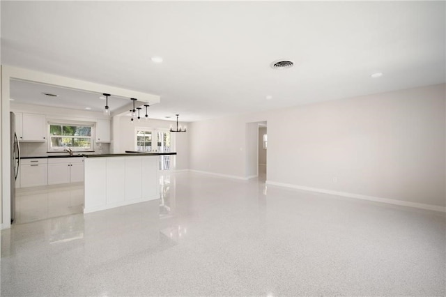 kitchen featuring stainless steel fridge, decorative light fixtures, sink, white cabinets, and a center island