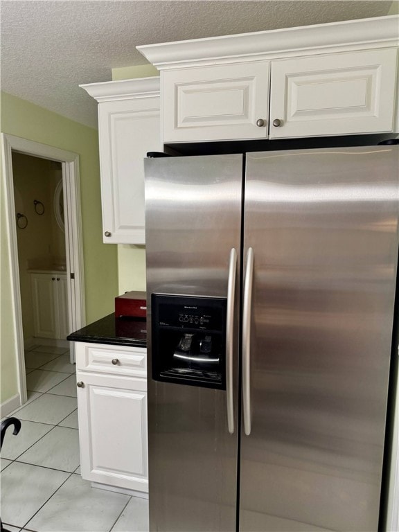 kitchen with stainless steel fridge, white cabinets, dark countertops, a textured ceiling, and light tile patterned flooring