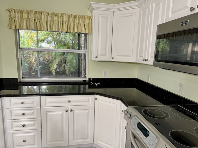 kitchen with stainless steel microwave, white cabinets, dark stone countertops, and range with electric stovetop