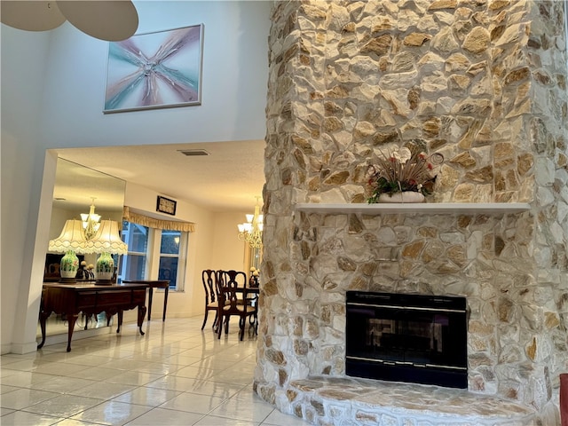 interior space featuring a textured ceiling, a stone fireplace, a notable chandelier, visible vents, and baseboards