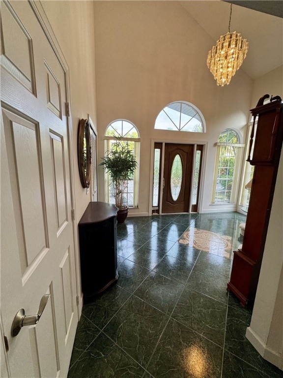 entryway with high vaulted ceiling, a wealth of natural light, baseboards, and an inviting chandelier