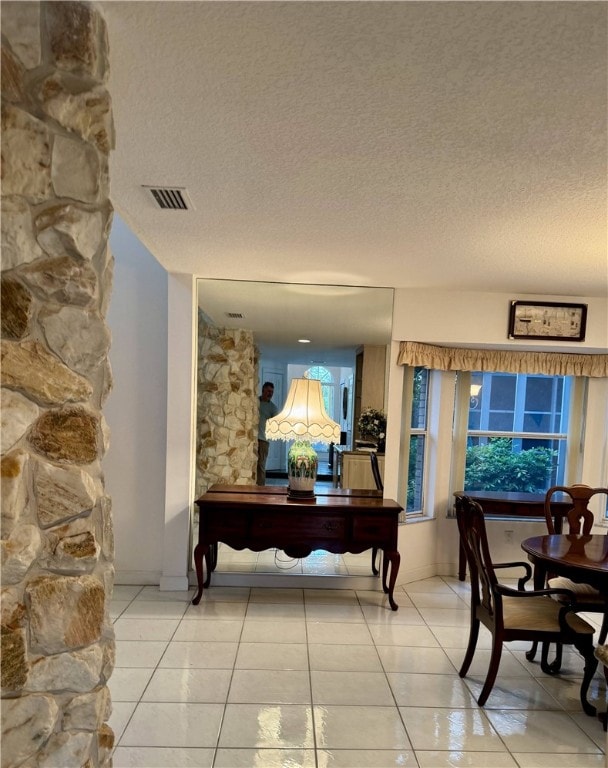 hall with light tile patterned floors, a textured ceiling, and visible vents