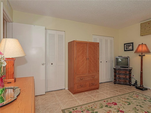 bedroom with a textured ceiling and multiple closets