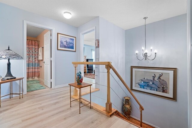 corridor featuring a textured ceiling, light hardwood / wood-style floors, and a notable chandelier