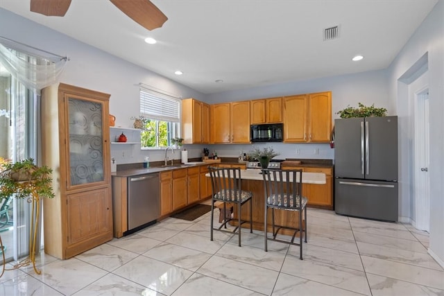 kitchen featuring appliances with stainless steel finishes, a kitchen breakfast bar, ceiling fan, sink, and a kitchen island