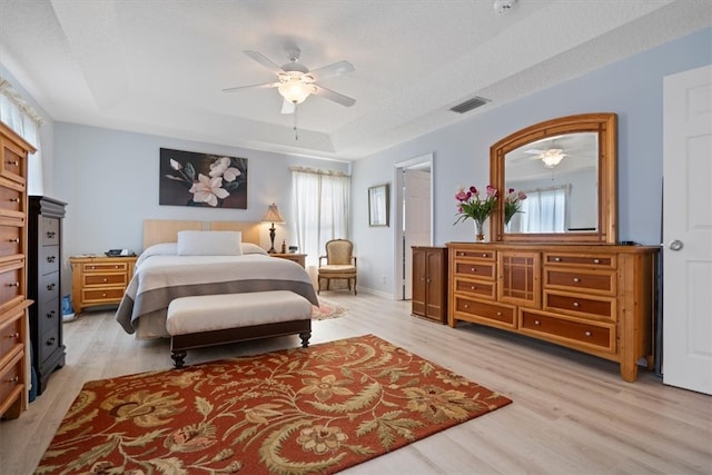 bedroom with a tray ceiling, ceiling fan, light hardwood / wood-style floors, and a textured ceiling