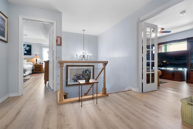 hall featuring light wood-type flooring, a textured ceiling, and an inviting chandelier