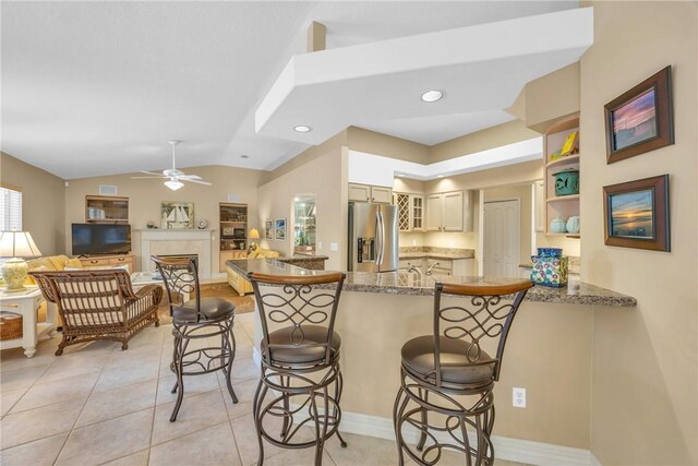 kitchen with stainless steel fridge, lofted ceiling, a breakfast bar area, a peninsula, and a fireplace