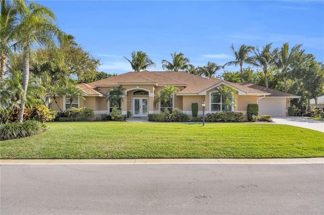 mediterranean / spanish-style house featuring driveway, stucco siding, a front yard, and french doors