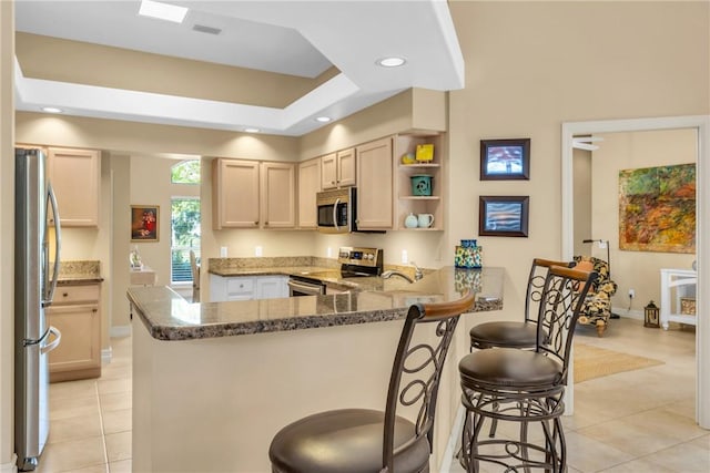 kitchen with dark stone counters, appliances with stainless steel finishes, a kitchen breakfast bar, a peninsula, and light tile patterned flooring