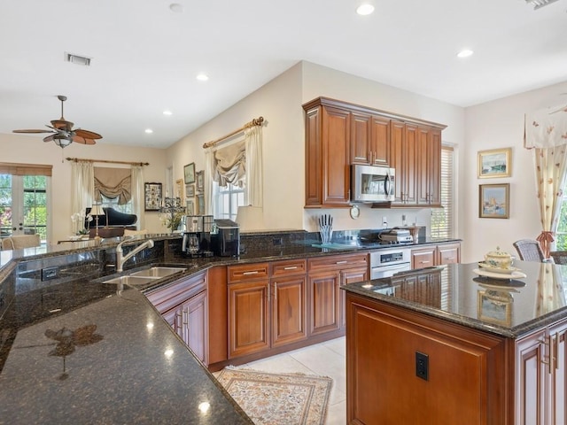 kitchen featuring stainless steel appliances, sink, light tile patterned floors, and dark stone counters