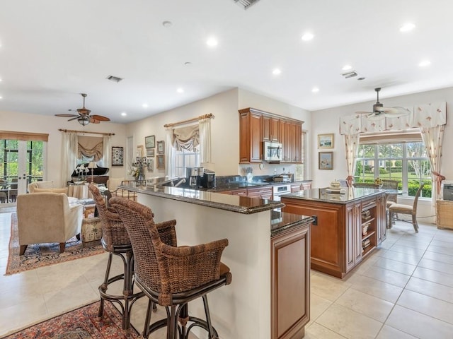 kitchen featuring light tile patterned floors, a breakfast bar, a center island, kitchen peninsula, and dark stone counters