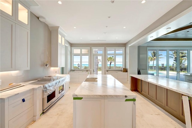 330 N Blue Wave Ln, Vero Beach, FL 32963 - kitchen with light stone countertops, a spacious island, glass insert cabinets, and white cabinets