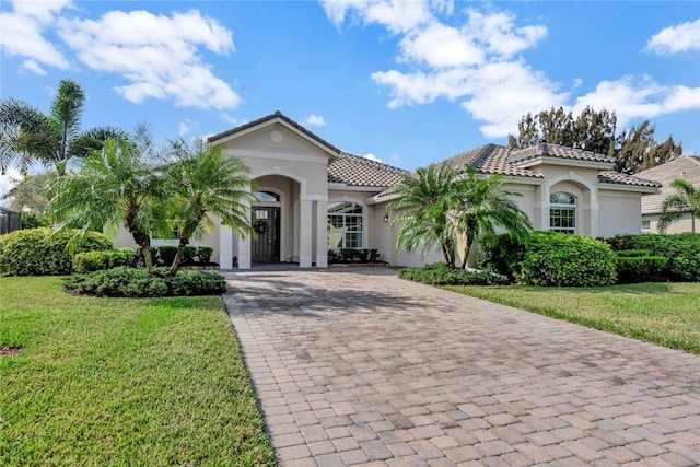 mediterranean / spanish-style house featuring decorative driveway, a tile roof, stucco siding, an attached garage, and a front lawn