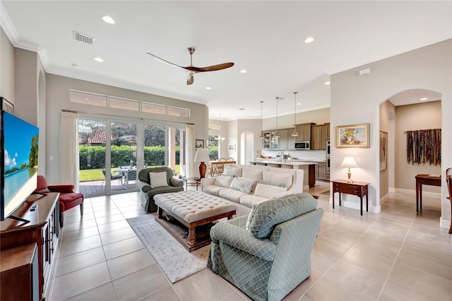 living area with arched walkways, crown molding, a ceiling fan, and recessed lighting