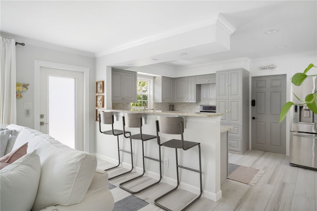 kitchen with gray cabinetry, stainless steel refrigerator with ice dispenser, backsplash, open floor plan, and a breakfast bar area