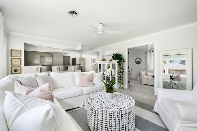 living room featuring visible vents, light wood-style floors, ornamental molding, and a ceiling fan