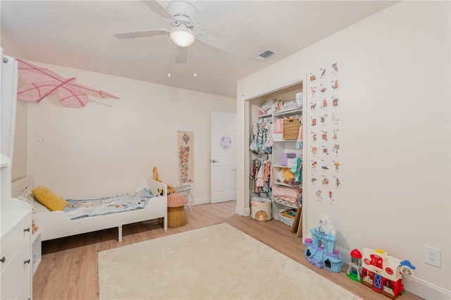 bedroom featuring a textured ceiling, a closet, light hardwood / wood-style flooring, and ceiling fan