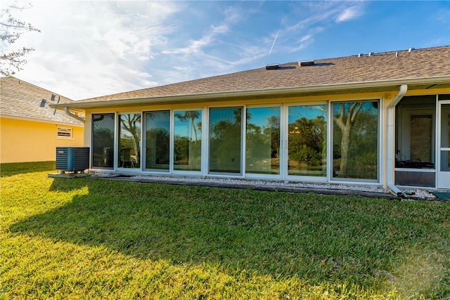 rear view of house with central AC unit and a lawn