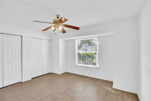 unfurnished bedroom featuring multiple closets, ceiling fan, and light hardwood / wood-style flooring