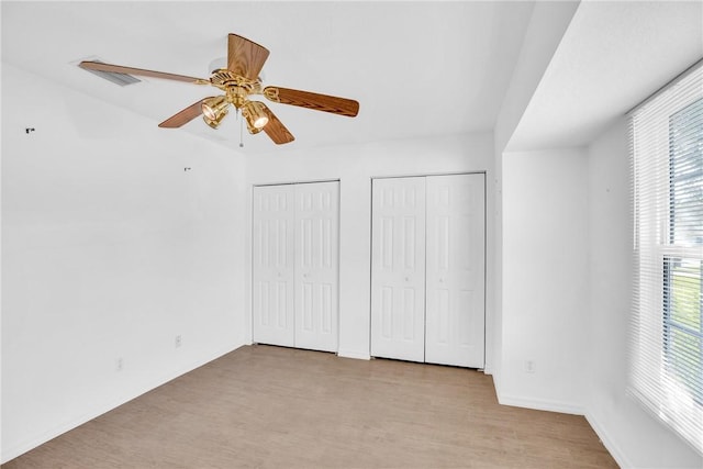 unfurnished bedroom with ceiling fan, light hardwood / wood-style floors, and multiple closets