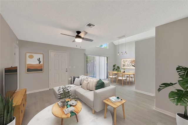 living room featuring ceiling fan with notable chandelier, light hardwood / wood-style floors, and a textured ceiling