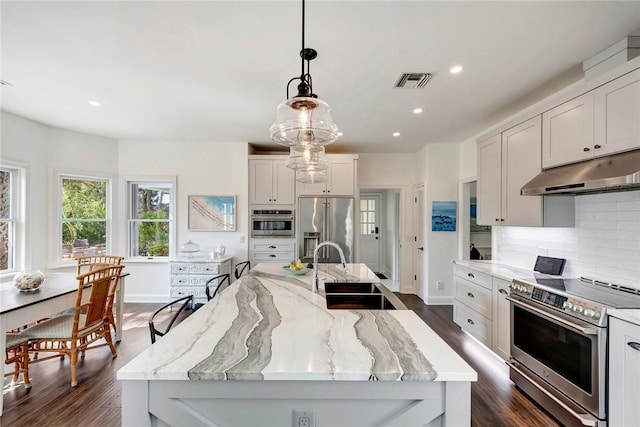 kitchen with sink, high end appliances, white cabinetry, decorative light fixtures, and a large island with sink