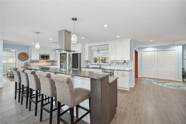 kitchen featuring white cabinets, stainless steel appliances, island exhaust hood, and hanging light fixtures