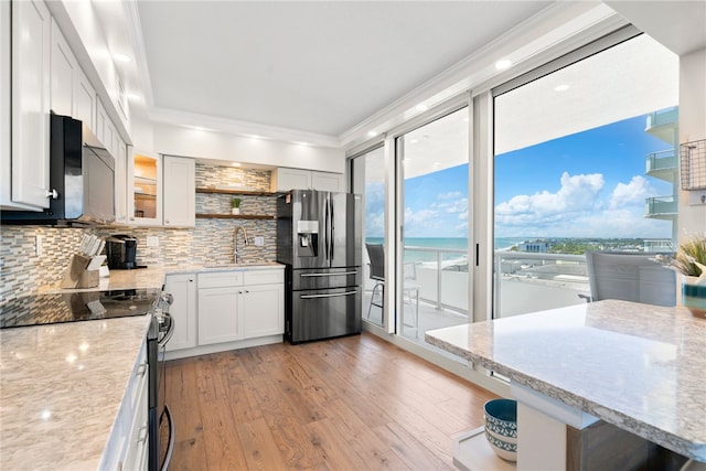 kitchen with stainless steel appliances, white cabinets, decorative backsplash, crown molding, and light hardwood / wood-style flooring