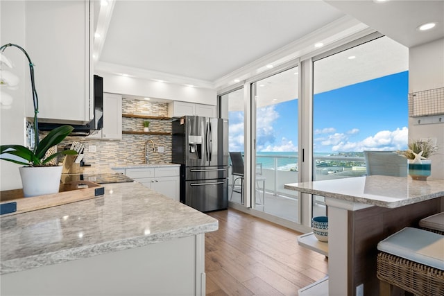 kitchen featuring a water view, light stone counters, white cabinets, stainless steel fridge with ice dispenser, and ornamental molding