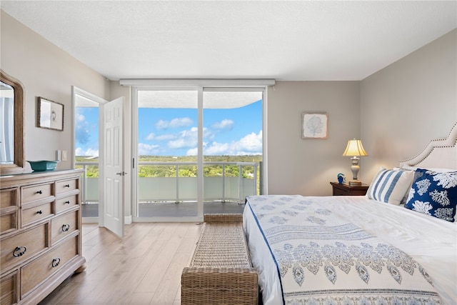 bedroom featuring a wall of windows, a textured ceiling, light hardwood / wood-style floors, and access to exterior