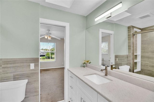 bathroom with tile walls, vanity, ceiling fan, toilet, and a shower with door