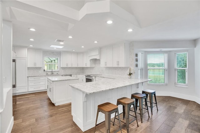 kitchen featuring stainless steel range with electric cooktop, a center island, a kitchen breakfast bar, decorative backsplash, and white cabinets