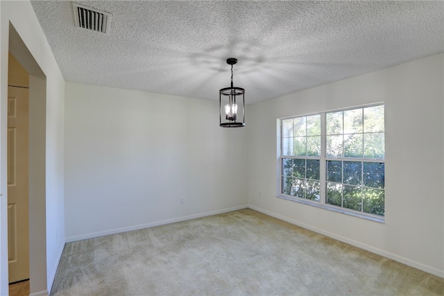 carpeted spare room featuring a textured ceiling and an inviting chandelier