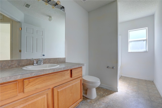 bathroom with toilet, vanity, a textured ceiling, and tile patterned floors