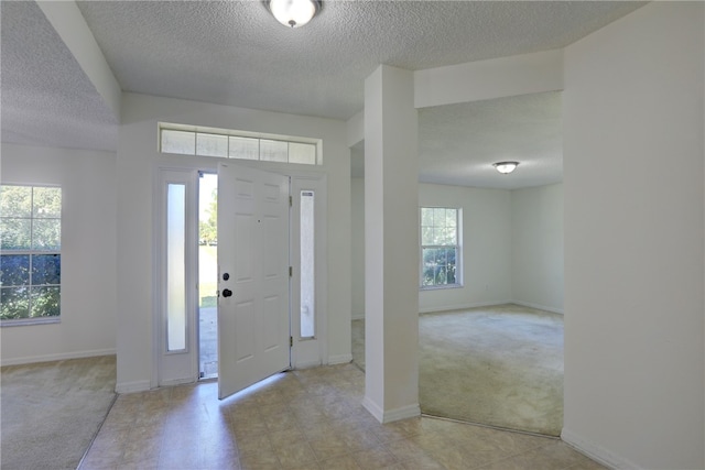 entryway with a textured ceiling, light colored carpet, and a healthy amount of sunlight