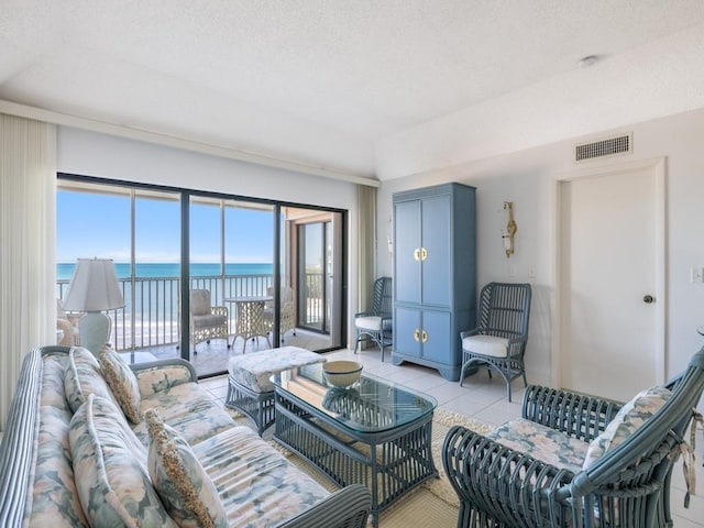 living room featuring visible vents, a water view, a textured ceiling, and light tile patterned floors