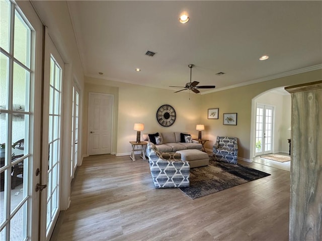 living area featuring visible vents, ornamental molding, arched walkways, light wood finished floors, and baseboards