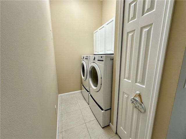 clothes washing area featuring light tile patterned floors, baseboards, cabinet space, and washing machine and dryer