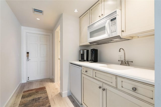 kitchen with a sink, light wood-style floors, baseboards, dishwasher, and white microwave