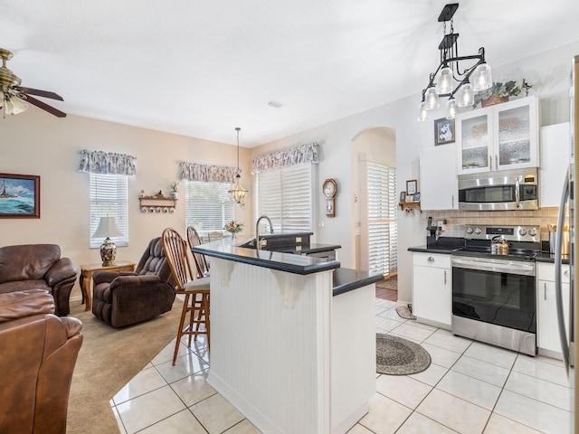 kitchen with stainless steel appliances, a kitchen breakfast bar, white cabinets, and decorative light fixtures