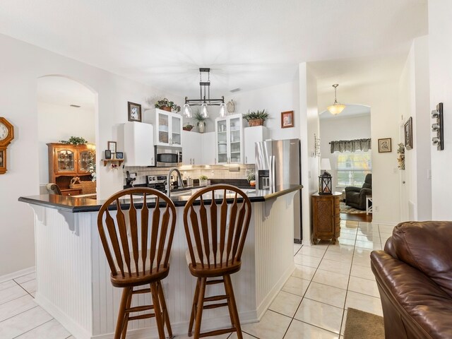 kitchen featuring stainless steel appliances, white cabinetry, tasteful backsplash, a breakfast bar area, and pendant lighting