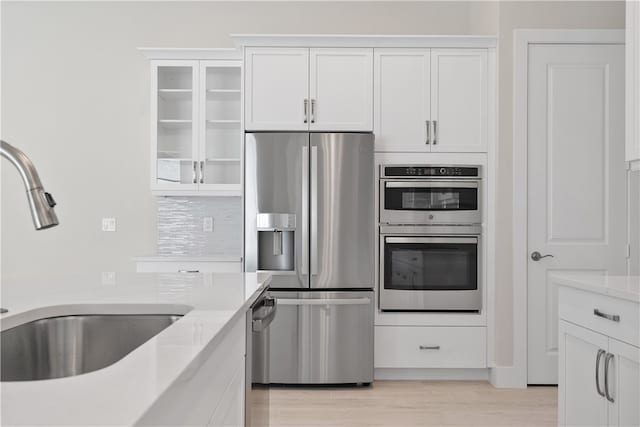 kitchen featuring sink, light wood-type flooring, light stone counters, white cabinetry, and stainless steel appliances