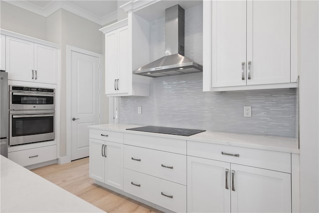 kitchen featuring white cabinets, wall chimney exhaust hood, black electric cooktop, light hardwood / wood-style floors, and stainless steel double oven