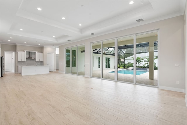 unfurnished living room with a raised ceiling, light wood-type flooring, and ornamental molding