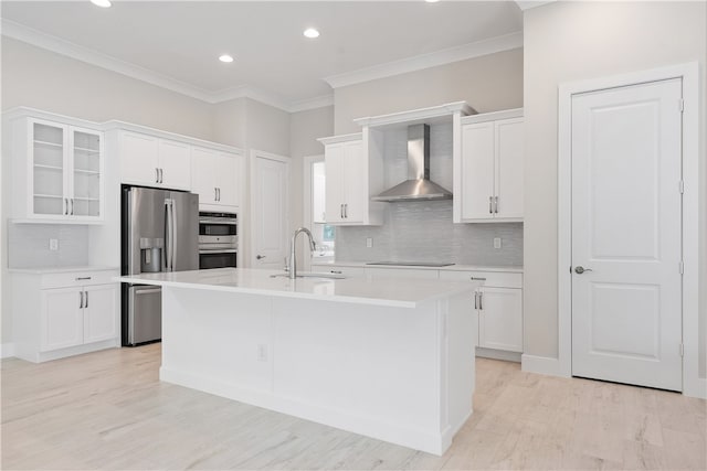 kitchen featuring appliances with stainless steel finishes, wall chimney exhaust hood, a kitchen island with sink, sink, and white cabinets