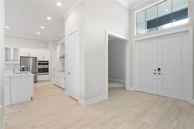 entrance foyer featuring a towering ceiling, light hardwood / wood-style floors, crown molding, and sink